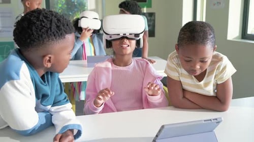 Una niña en edad escolar se pone unos auriculares VR blancos en la mesa de clase, sus compañeros señalan la tableta y aprenden
