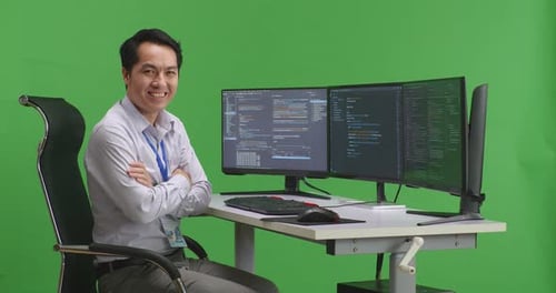 Developer Crossing Arms And Smiling To Camera While Write Code With Multiple Screens In Green Screen