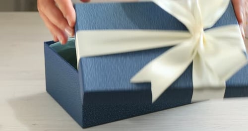 Opening Blue Gift Box with White Ribbon Indoors