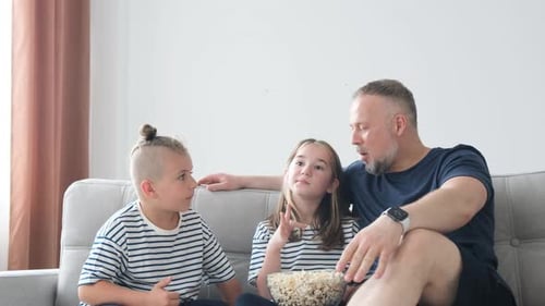 Father with Son and Daughter Eating Popcorn on Couch