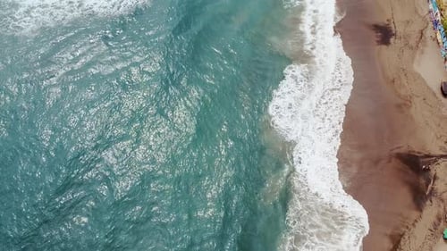 Aerial of clear turquoise picturesque ocean waves crashing onto shore of white beautiful sandy beach