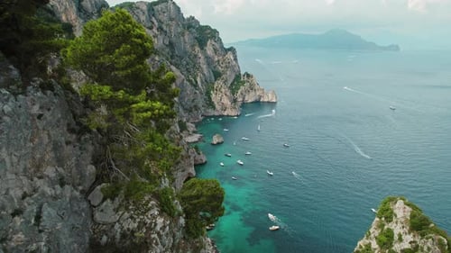 A lush green coastline with boats and a prominent rocky formation jutting out. Aerial view of summer
