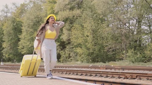 Brunette Woman Walking with Yellow Suitcase at Train Station