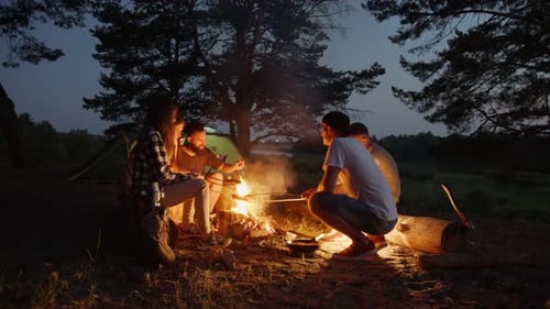Hipster Man and a Young Beautiful Girl Prepare a Picnic Lunch While Friends Play Ball Near a Pine