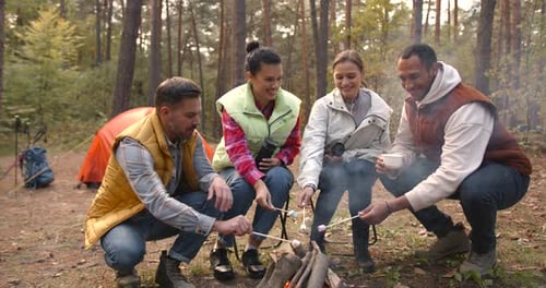 Amigos asando melosidades de pantano en palitos en una hoguera y divirtiéndose en Camp Fire