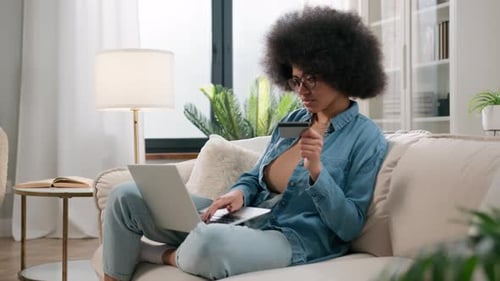 African American Ethnic Girl Making Online Payment Holding Bank Credit Card Using Modern Laptop at