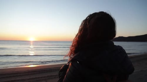 Silhouette of girl watching romantic sunset with yellow sun on bright sky reflecting sunlight on sea