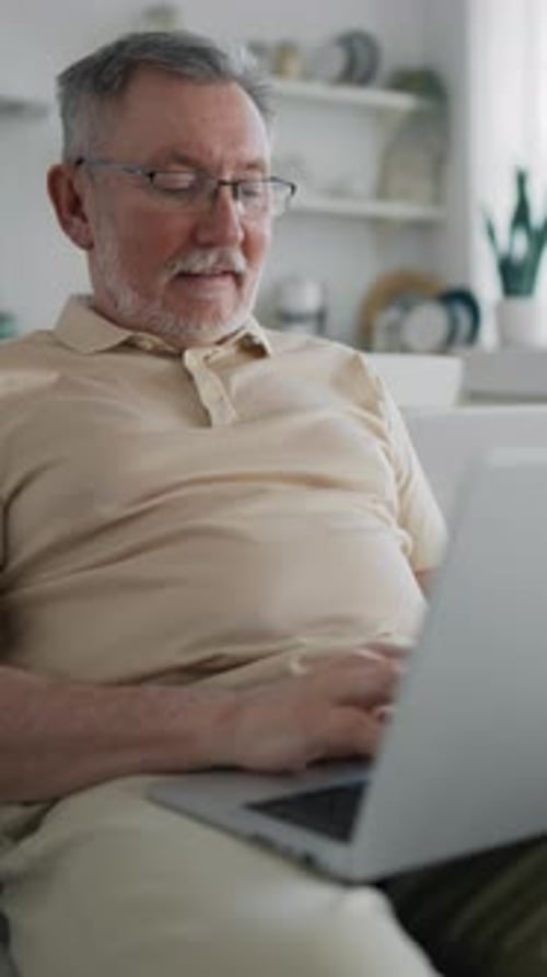 Senior Man Uses Laptop at Home During the Day