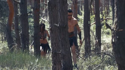 Female and male ancient warriors with weapons are walking through the forest
