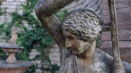 Ancient weathered female stone garden Statue In decorative botanical blossoming garden.