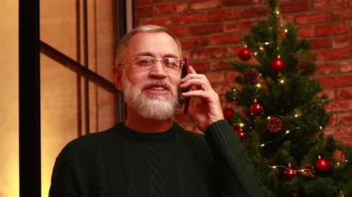 an Elderly Man in a Green Knitted Talking with Family By Phone Video Connection Near the Christmas
