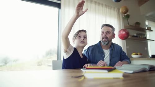 Mature Father with Small Son Sitting at Table Indoors, Working on School