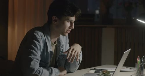 Young Man Making Online Video Call with Laptop Computer at Desk in Office at Night