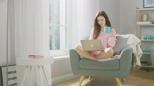 Portrait of Young Brunette Works on Laptop Computer while Holding Cup with Hot Beverage, and Drink
