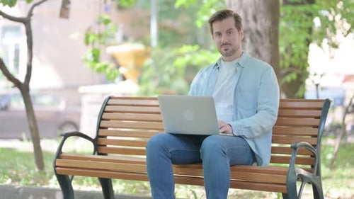 Man Using Laptop on Bench in Park