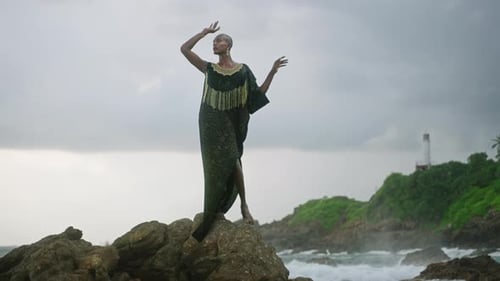 LGBTQ Bipoc Person in Luxury Dress Boutique Golden Jewelry Poses Against Lighthouse on Cliff Ocean