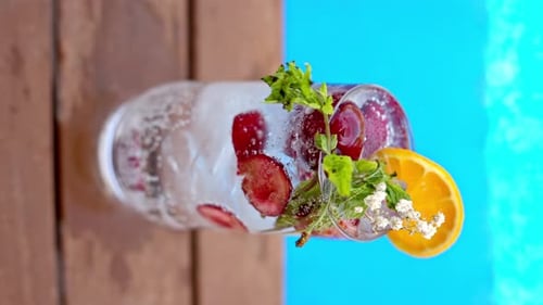 Mojito cocktail glass with ice and cherry and mint, soda and gin near a blue pool close up