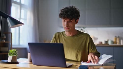 Smiling Man Works at Laptop with Book