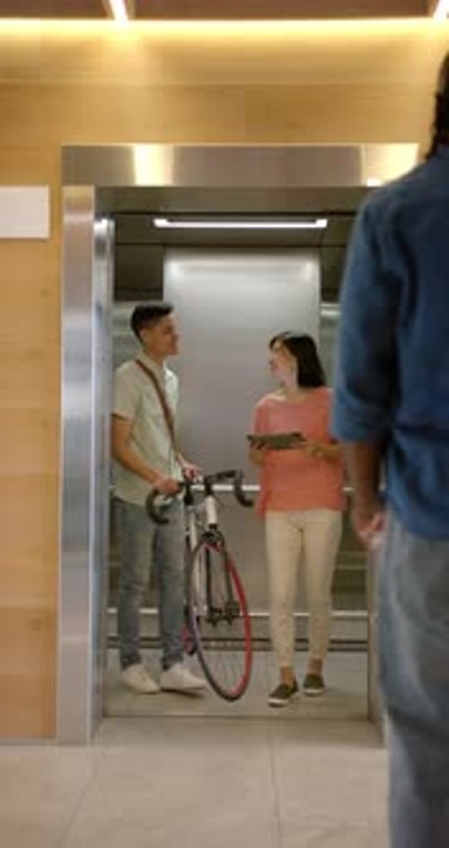 Young Adults Exiting Elevator with Bicycle and Tablet