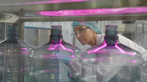 Une travailleuse inspecte la qualité de l'eau et des bouteilles dans une usine de production d'eau potable