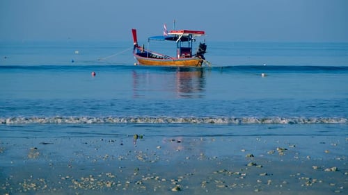 One colorful Thai boat tag at the beach with blue sea and waves splashing to the shore