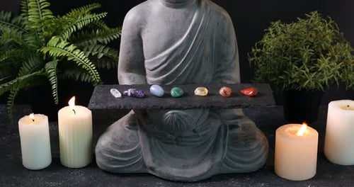 Estátua com pedras preciosas de chakra e velas acesas na mesa preta, closeup