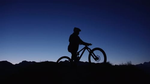 A mountain biker is posing at the top of a mountain at sunrise