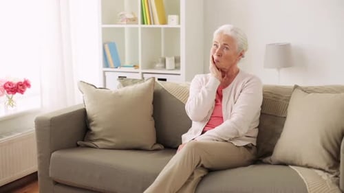 Worried senior woman sitting on sofa indoors