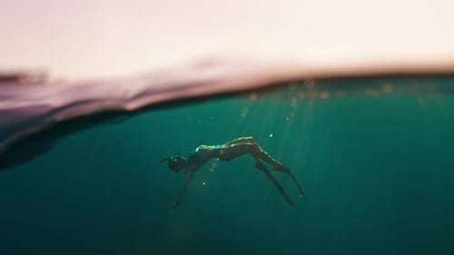 Woman freediver swims underwater in the sea at sunset and relaxes and floats beneath the surface