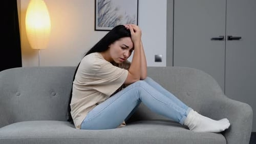 Sad Young Woman Sitting on Couch at Home