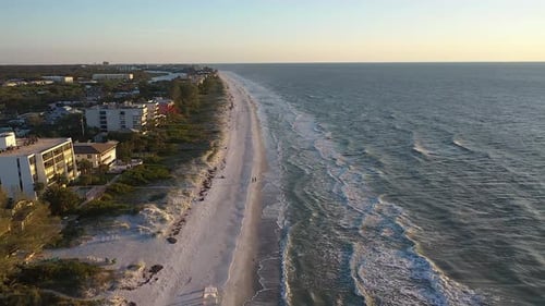 Foto aérea da praia ao pôr do sol, ondas chegando à costa
