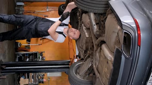 Mechanic Working Under a Car in Garage Inspecting Wheel and Tire