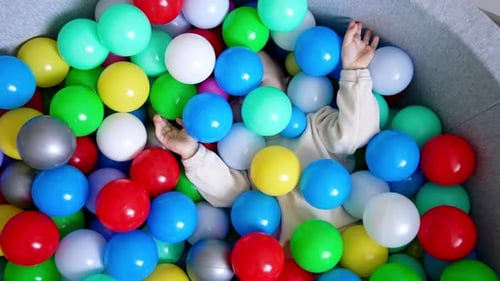 Baby boy lies hiding in the colorful balls in a dry pool.