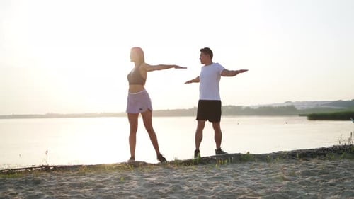 Young Woman and Man Stretching on Beach at Sunset