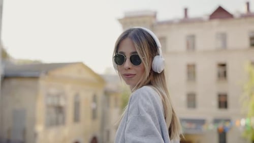 Woman in Modern Wireless Headphones Listening Music While Walking Outdoors