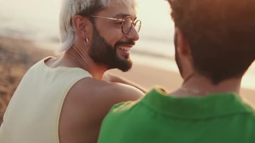 De perto, casal homossexual apaixonado passa tempo juntos sentados na praia ao nascer do sol