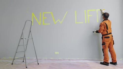 A Male Worker Makes Repairs Painting the Wall with a Brush Word New Life