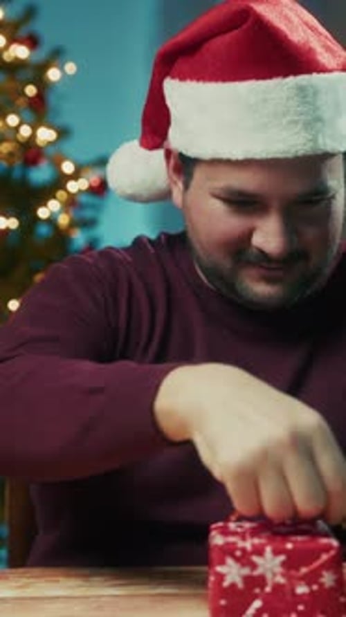 Young Man Wraps Christmas Gift On Table On Magical Night Against The Tree