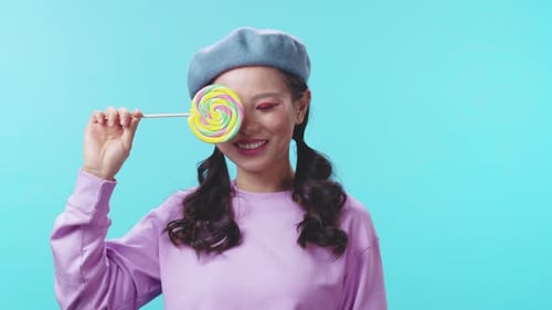 Une jeune femme espiègle tenant joyeusement une sucette colorée dans un cadre lumineux et dynamique