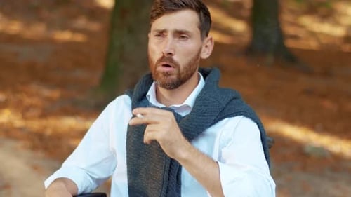 Close Up Face Sad Attractive Young Man in Wheelchair Smoking Cigarette in Beautiful Park at Sunlight