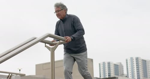 Homem sênior se aproximando do corrimão da escada, subindo e estendendo os braços para se aquecer no terraço