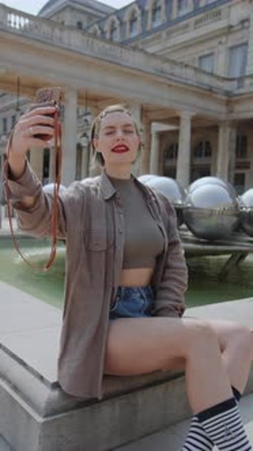 Eine Frau sitzt auf einer Steinbank und macht ein Selfie mit ihrem Smartphone