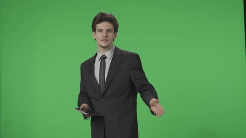 Un presentador de un programa de previsión meteorológica de televisión está de pie con una tableta en la mano y señala una pantalla verde
