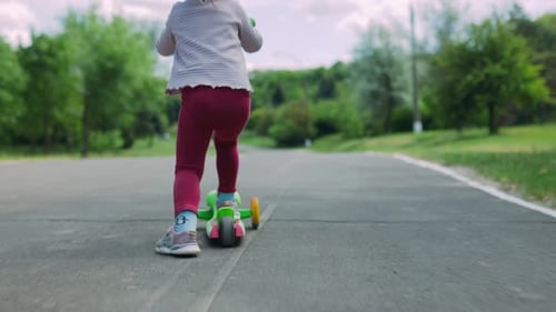 Child Rides Scooter Down Path in Park