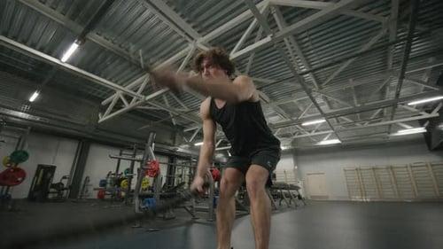 Muscular Man Performing Battle Rope Exercise while Training in Gym