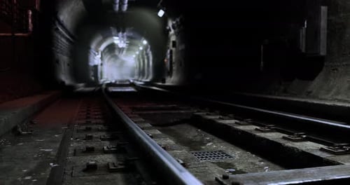 Dark Underground Tunnel with Train Tracks Illuminated By Distant Lights