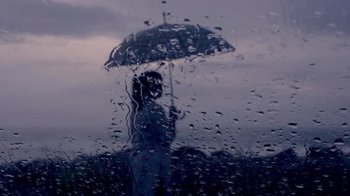 Raindrops trickling down on wet clear car window glass during heavy rain against beach view , a lady