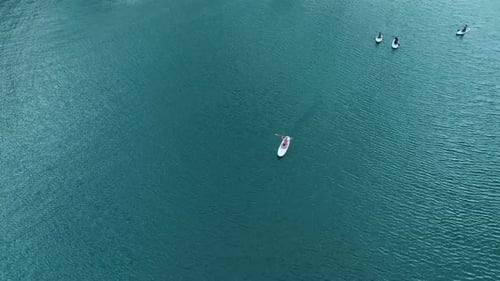 Aerial View Paddleboarding Through Emerald Waters Surrounded By Rugged Peaks and Unique Dry Trees