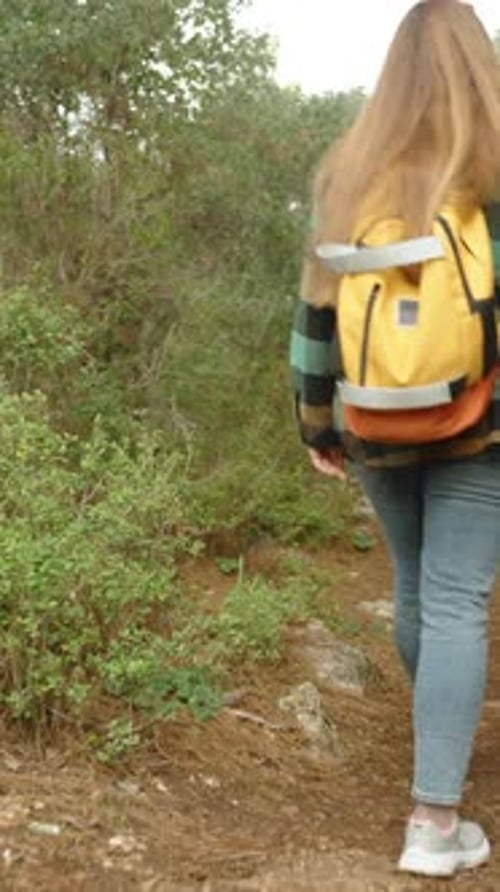 Vertical video. Young Woman Makes Her Way Through the Dense Forest Down the Mountain.