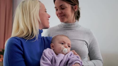 Happy gay lesbian couple and baby infant having tender moment at home - LGBTQ family and mothers